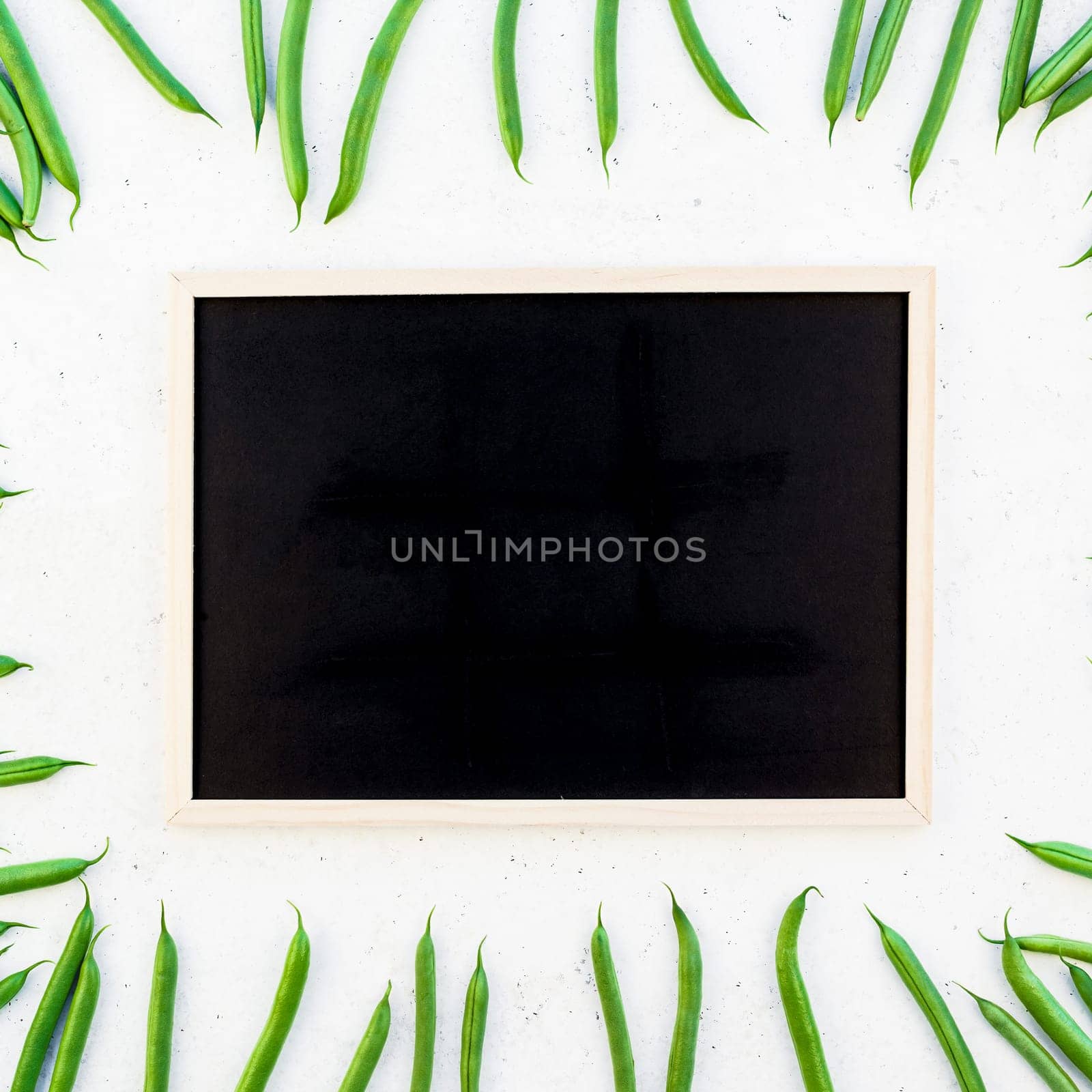 Creative scandinavian style flat lay top view of fresh green beans with blackboard on white concrete table background copy space. Minimal house cooking concept template for blog or recipe book