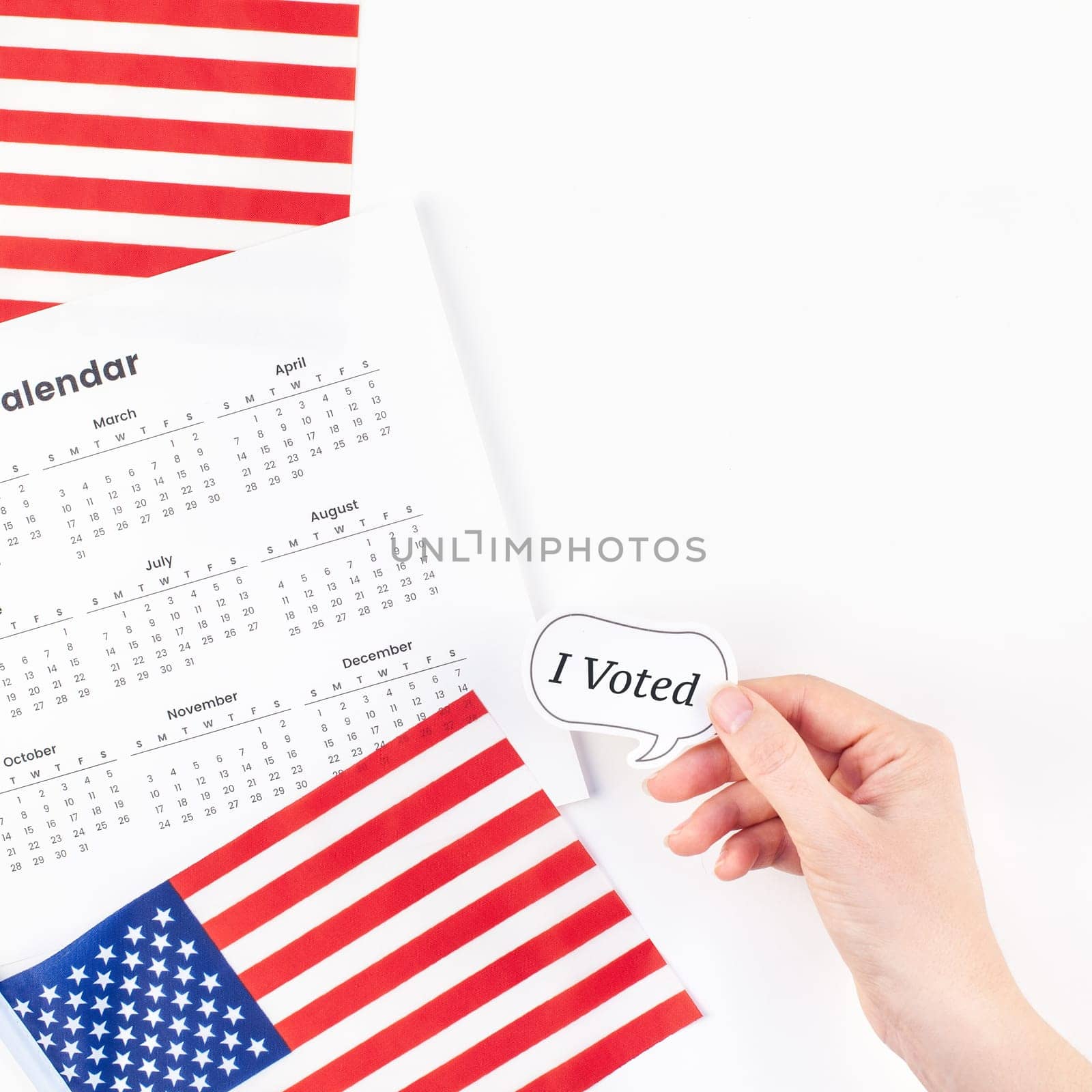 Creative top view flat lay of American flags for Elections Day with sticker I voted in hand with calendar copy space on white background in minimal style. Concept of patriotism and independence