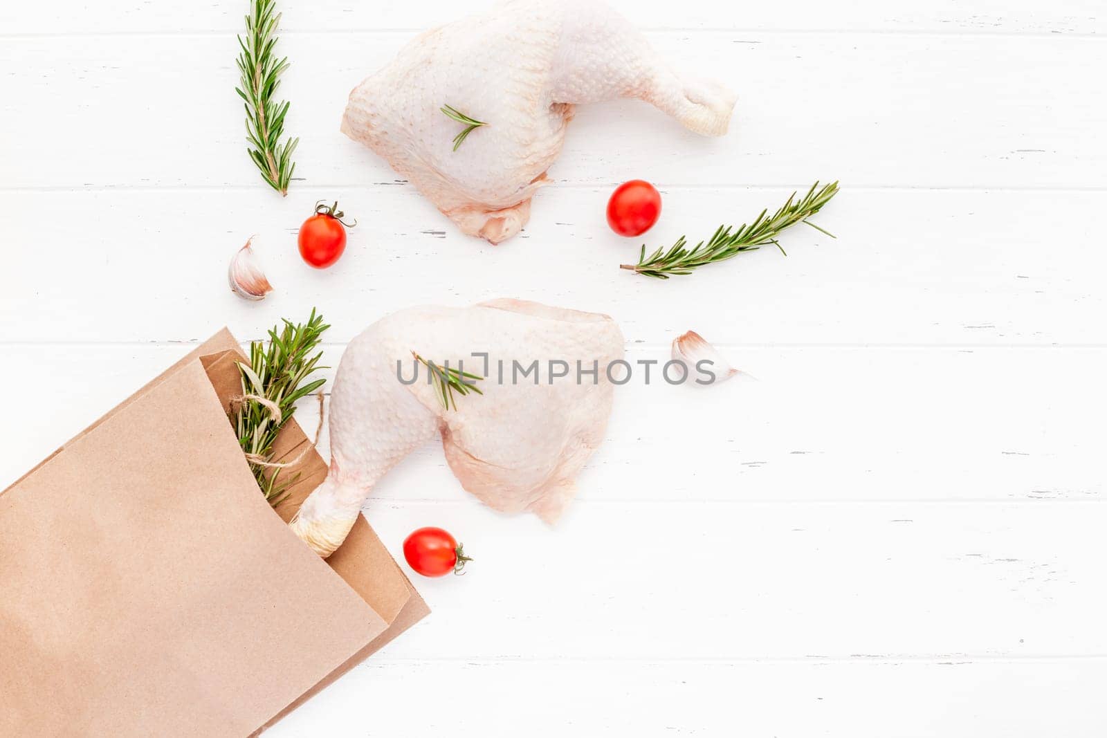 Creative Top view flat lay of fresh raw chicken legs with rosemary herbs garlic tomatoes on white wooden background with copy space. Food preparation recipe cooking concept