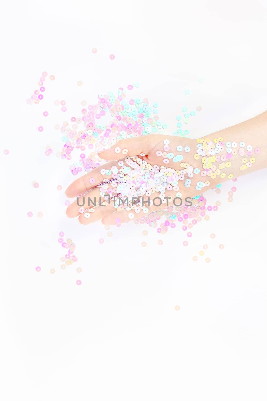 Pearl pastel confetti sparkles with woman hand on white background. Creative conceptual top view flat lay backdrop for your blog, text or design