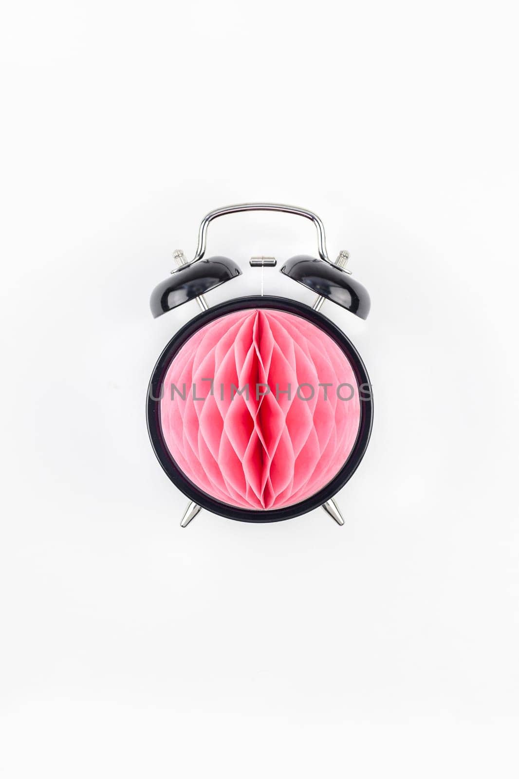 Birthday or baby shower party invitation card template. Black alarm clock with pink honeycomb paper ball on white background. Creative conceptual top view flat lay composition in minimal style