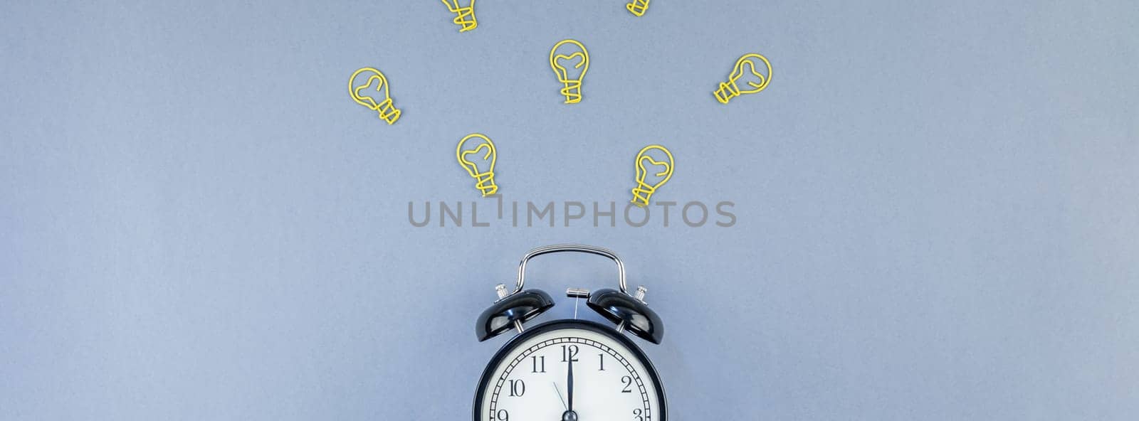 Top view flat lay of desk with black alarm clock and bulbs idea signs with copy space on blue background in minimal style. Concept of creativity, new plans, brainstorming, creative work