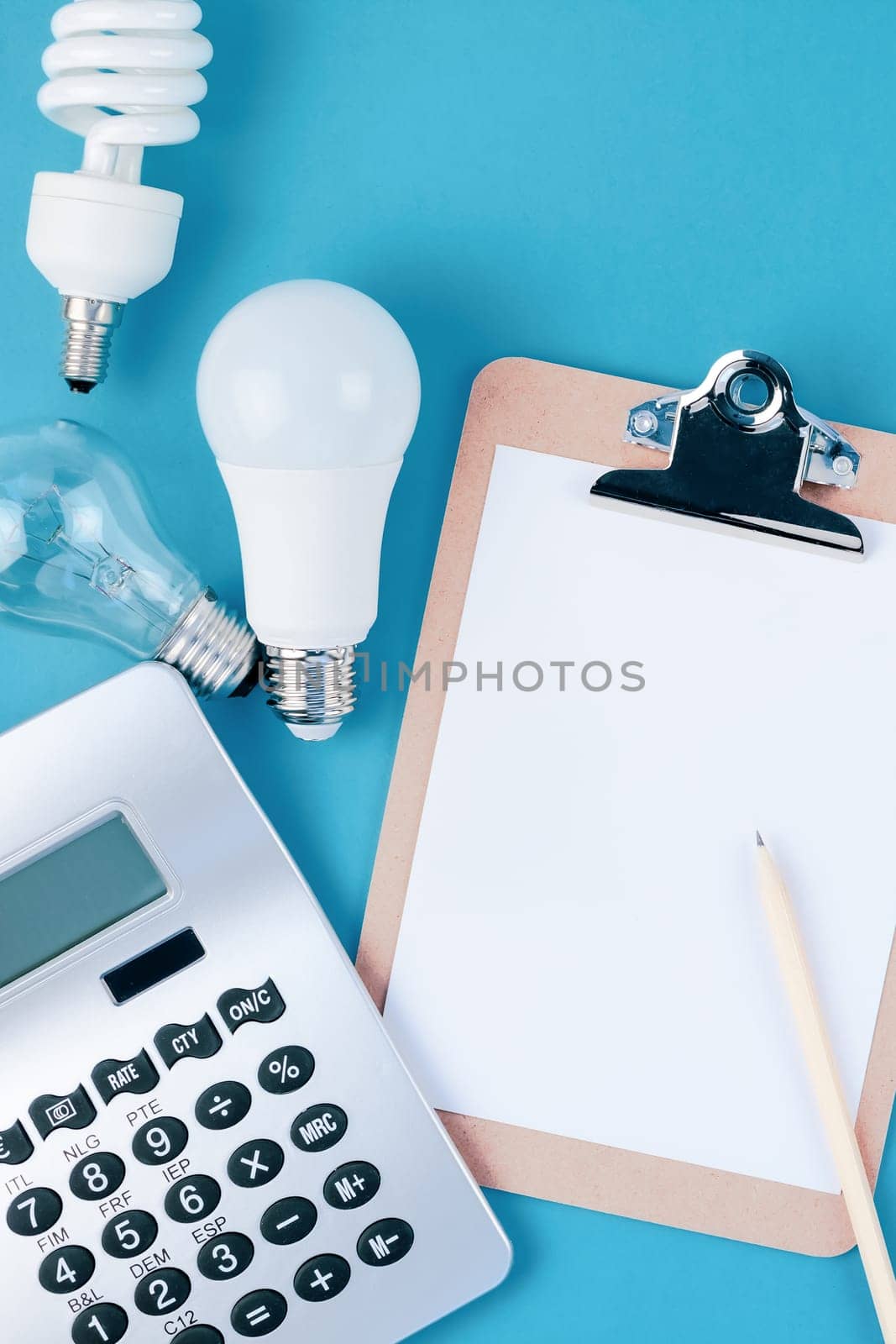 Energy and money saving and eco-friendly life in conceptual composition. Creative top view flat lay of new and old light bulbs calculator and clipboard with copy space on blue background minimal style
