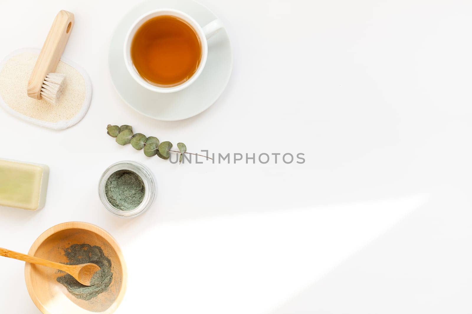 Spa, beauty cosmetics and body care treatment concept with copy space. Creative top view flat lay composition with cup of tea, green spirulina cleansing mask in wooden bowl on white background