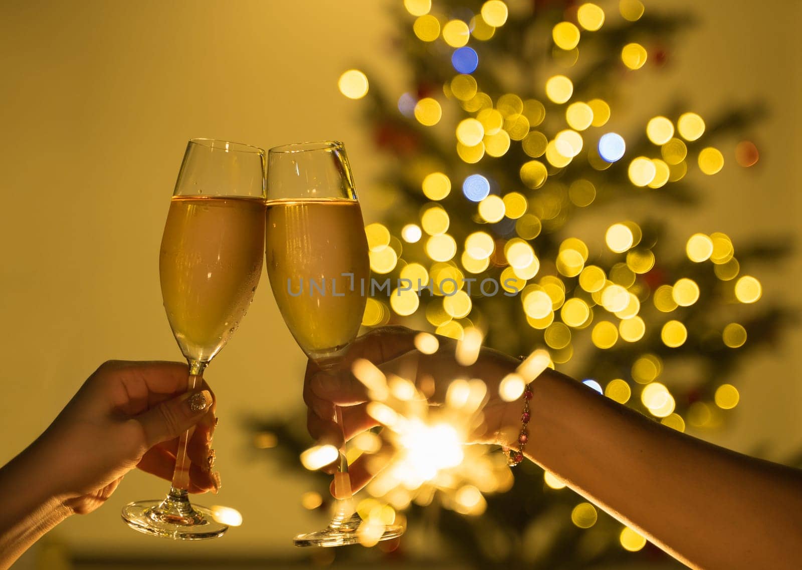 Two hands clinking champagne glasses in celebration party toast with a sparkling bokeh of Christmas lights and festive tree in the background