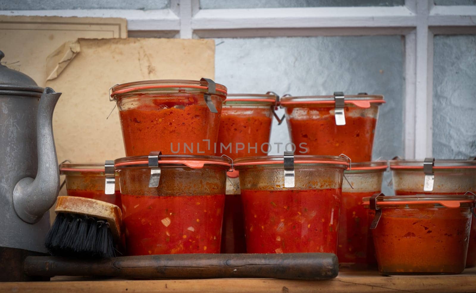 A row of glass jars filled with red sauce sit on a wooden table. The jars are of various sizes and are arranged in a neat row. Concept of abundance and abundance of food