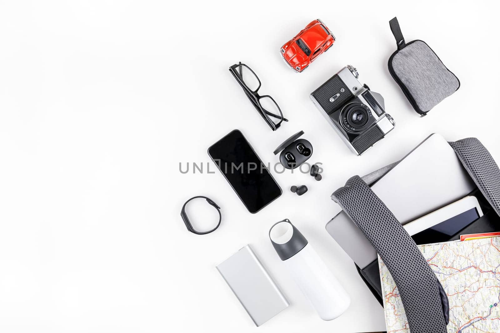 Creative top view flat lay of open backpack with laptop and tablet inside, mobile phone map copy space white background minimal style. Concept of modern man accessories for travel adventures and life