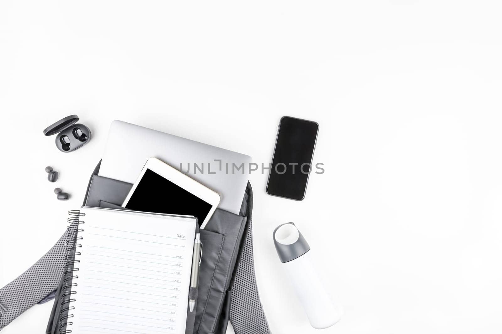 Creative top view flat lay of open backpack with laptop and tablet inside, mobile phone, copy space white background minimal style. Concept of modern man accessories for education, business and life