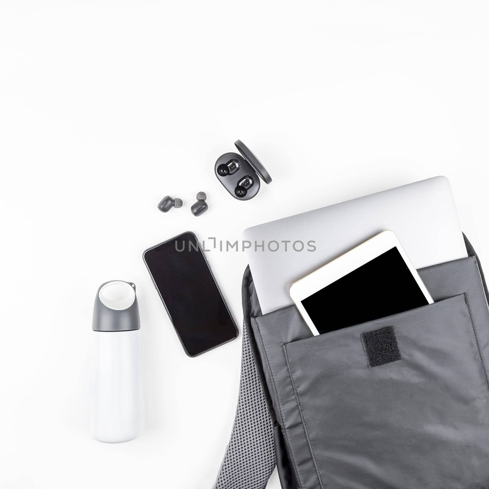 Creative top view flat lay of open backpack with laptop and tablet inside, mobile phone, copy space white background minimal style. Concept of modern man accessories for education, business and life