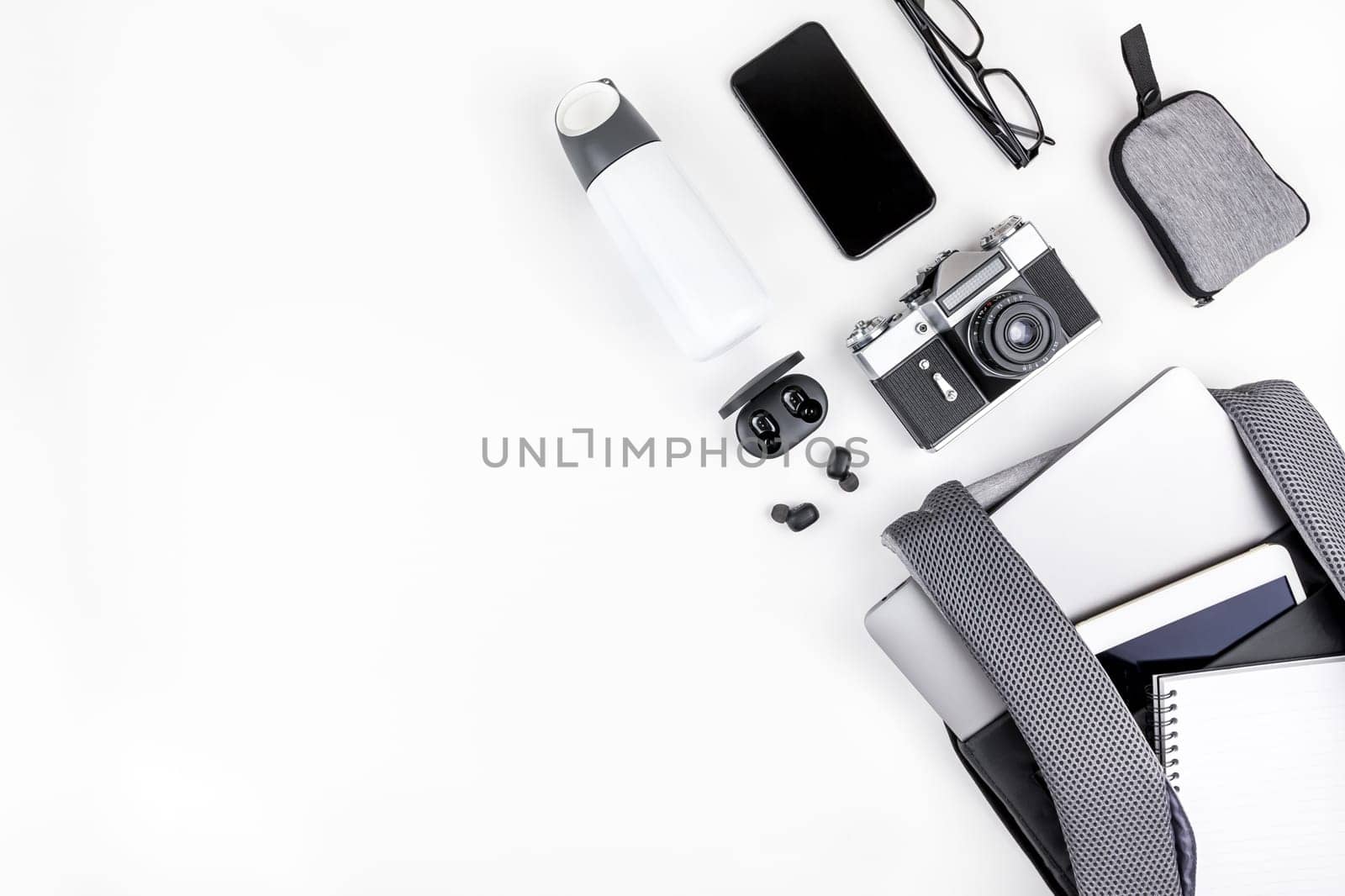 Creative top view flat lay of open backpack with laptop and tablet inside, mobile phone, copy space white background minimal style. Concept of modern man accessories for education, business and life