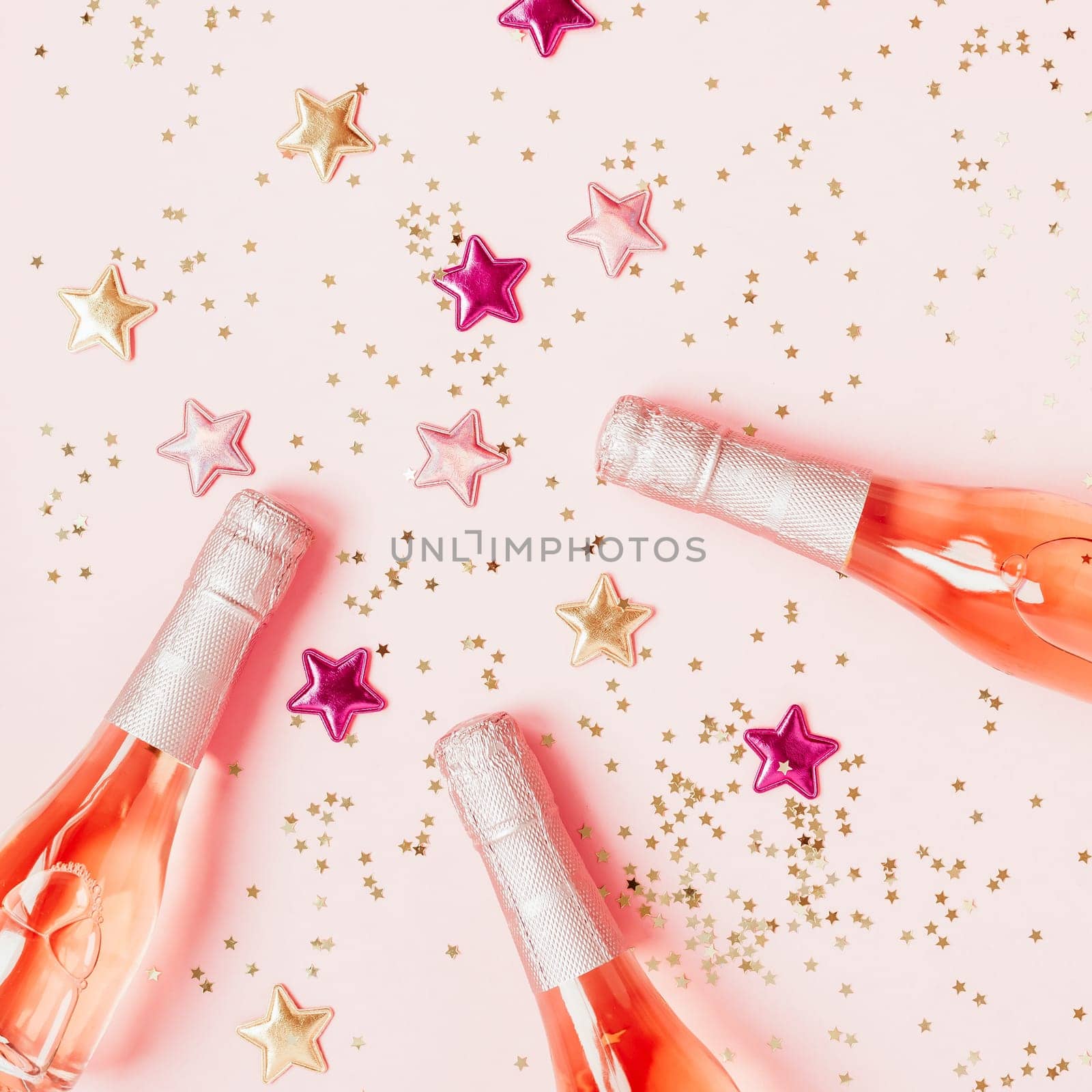 Christmas or New Year composition with bottles of rose champagne and golden shiny sparkle star confetti on pastel pink background, top view. Celebration flat lay. Party creative concept