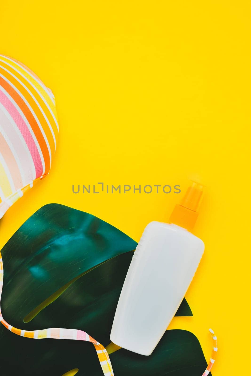 Tropical jungle palm monstera leaves, sunglasses, sunscreen blank bottle mockup and woman's swimsuit top on bright yellow paper background. Summer vacations creative flat lay concept template for text
