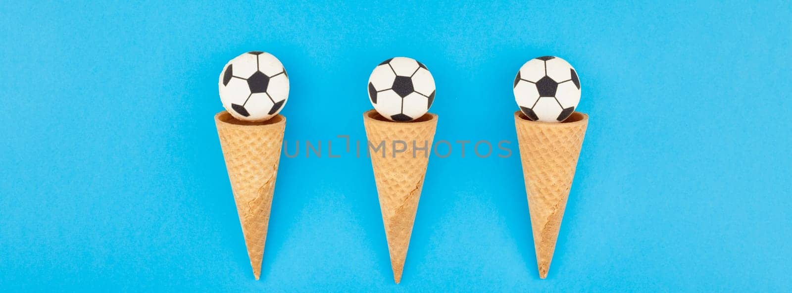 Long wide banner top view of ice cream waffle cones with soccer balls macarons on bright bold blue background with copy space in minimal style, concept of football games for children birthday