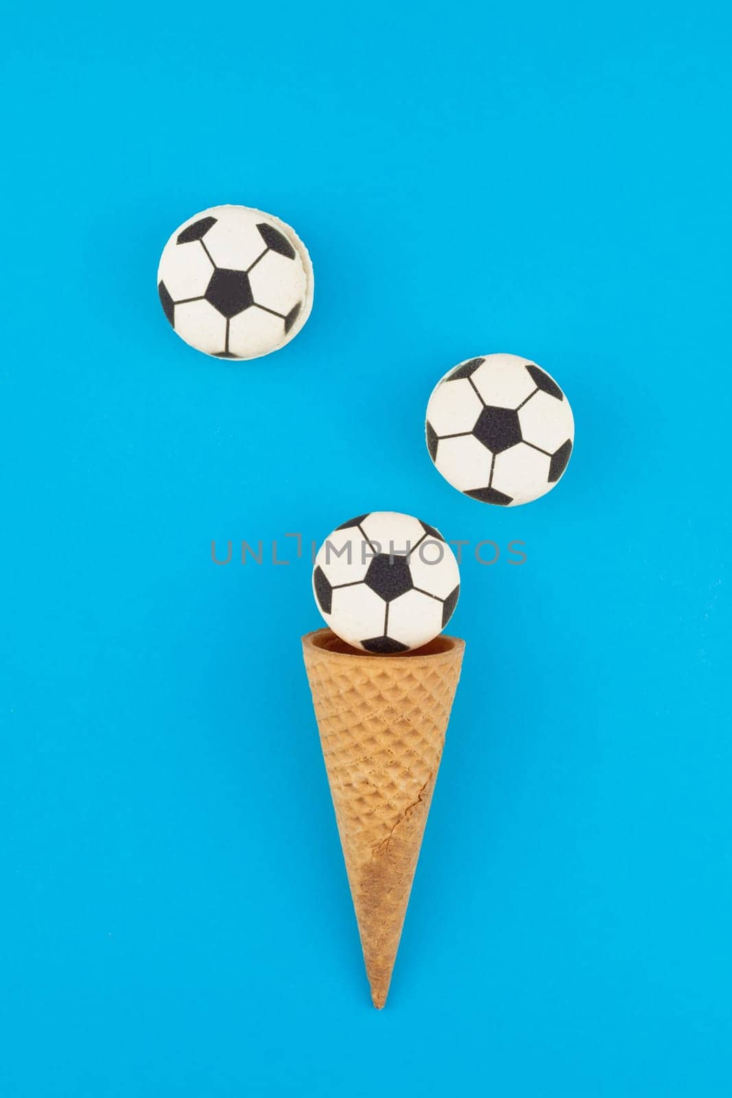 Creative flat lay top view of ice cream waffle cones with soccer balls macarons on bright bold blue background with copy space in minimal style, concept of football games for children birthday