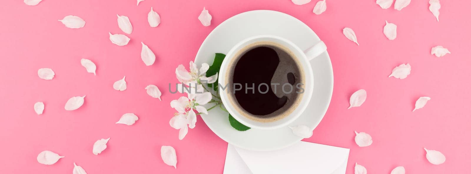 Creative flat lay concept top view of coffee cup and white apple tree flowers petals on pastel pink background with postcard mock up and copy space in minimal style template for text. Long wide banner