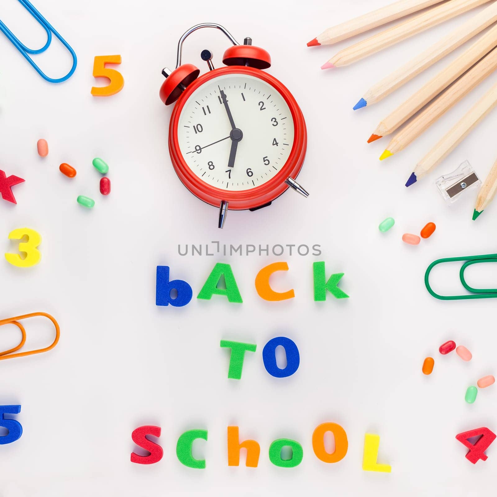 Square flat lay back to school concept with alarm clock, color school and office supplies on white table background with copy space, frame, template for text or design