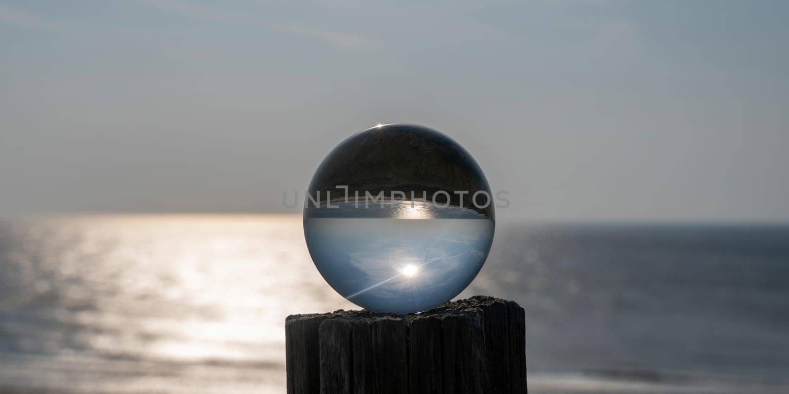Glass ball lies on a wooden post, in the ball the sea, the sun and the blue sky are reflected