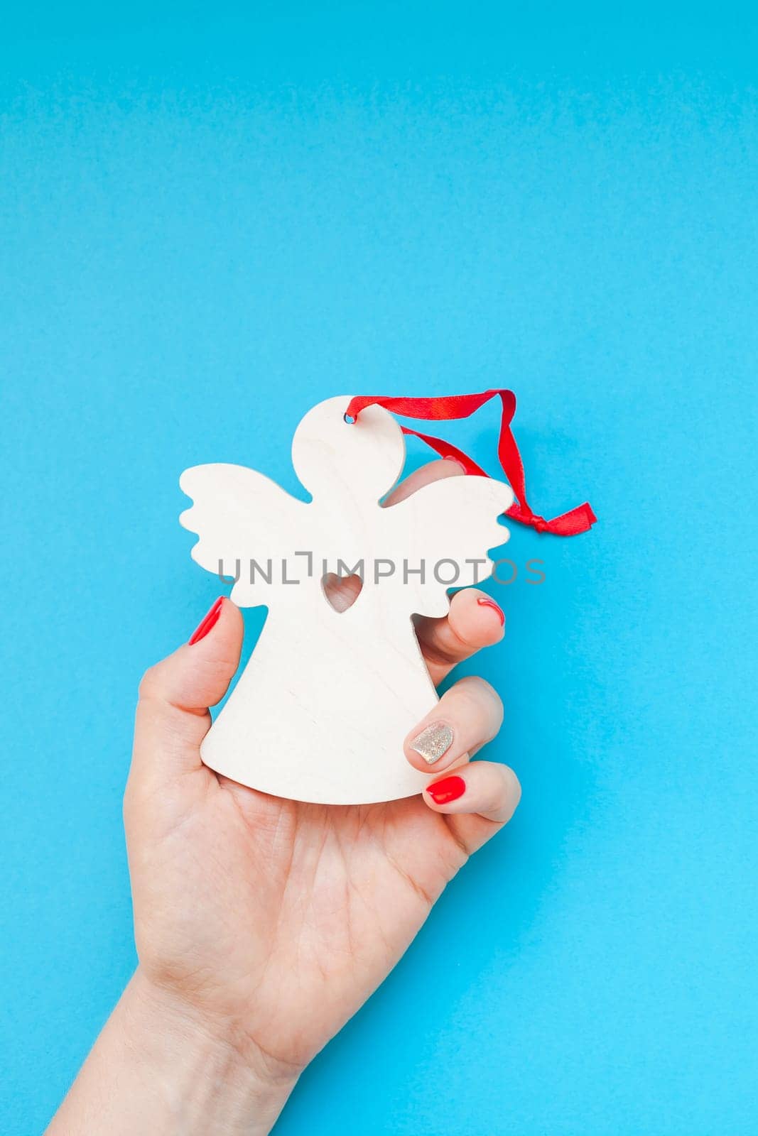 New Year or Christmas top view Xmas holiday celebration woman hand red manicure holding homemade wooden angel toy copy space turquoise blue color paper background minimal style. Template greeting card