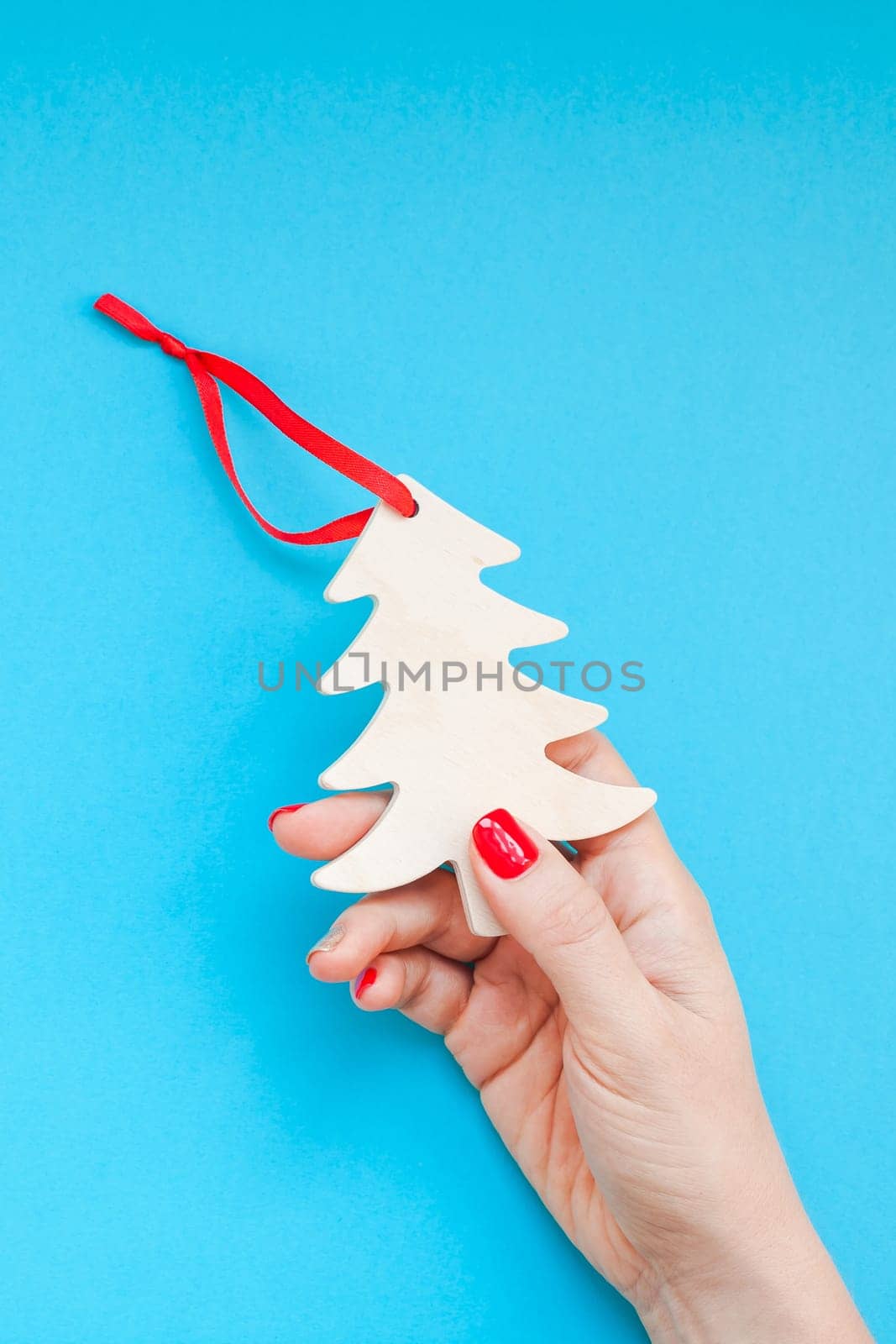 New Year Christmas top view Xmas holiday celebration woman hand red manicure holding homemade wooden fir tree toy copy space turquoise blue color paper background minimal style. Template greeting card