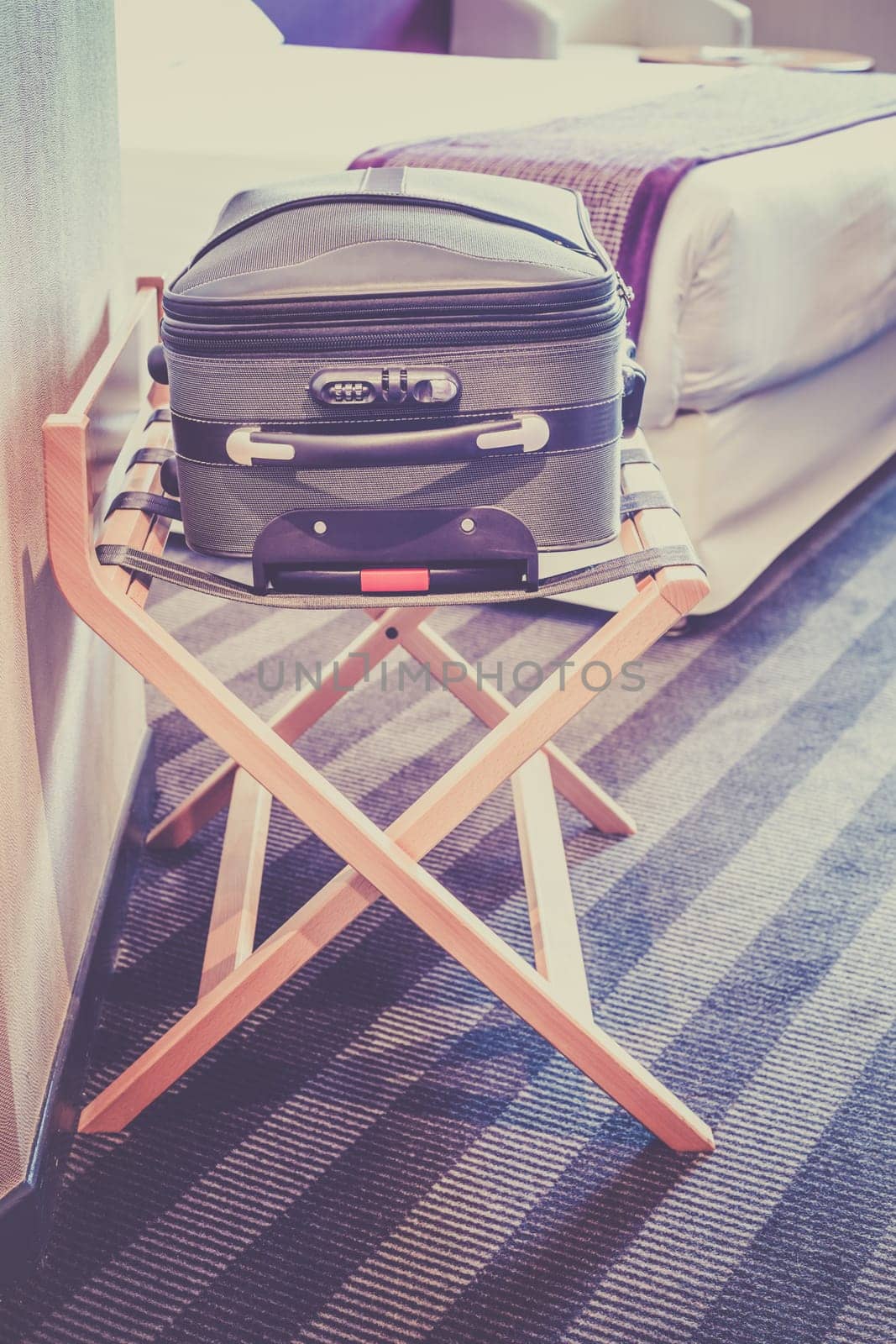 Hotel room with a suitcase on the luggage place and the bed. Filtered shot
