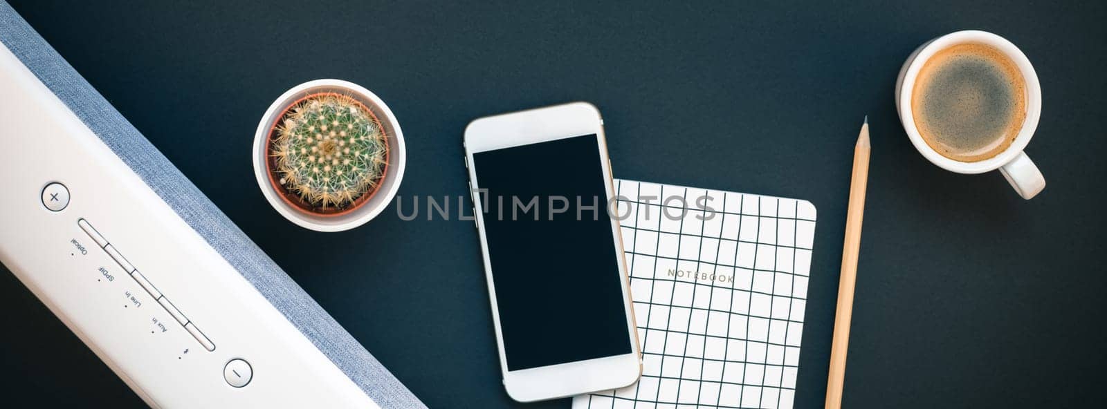 Top view flat lay of feminine desk workspace with white stereo bluetooth soundbar and smartphone for music listening and coffee cup with copy space on black background. Template for blog social media