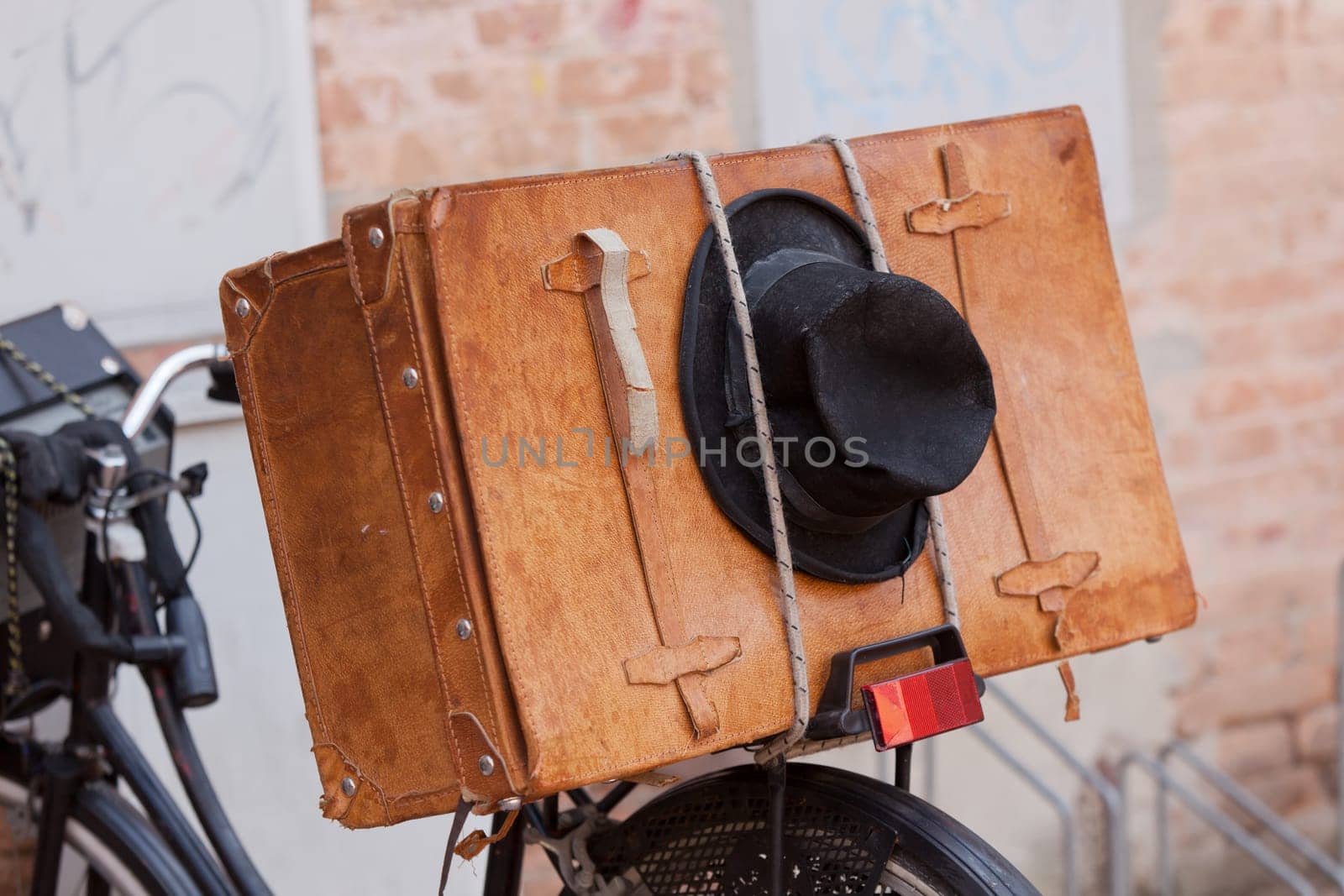 Shabby black hat and brown suitcase on the old bike. Horizontal image