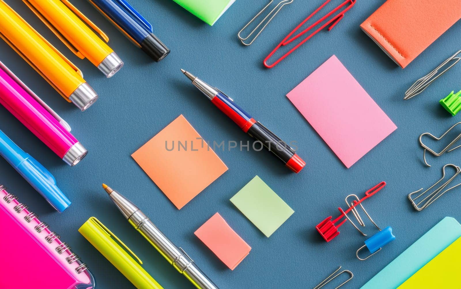 Vibrant stationery items including pens, sticky notes, and paper clips arranged on bright blue background, perfect for back to school or office organization concepts.