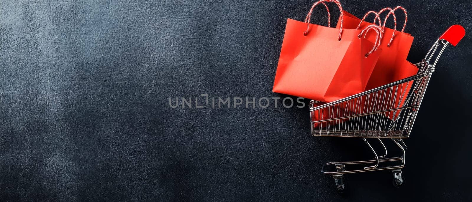 Miniature shopping cart containing red paper bags on dark textured background. Retail and e-commerce concept with copy space for Black Friday or sale.