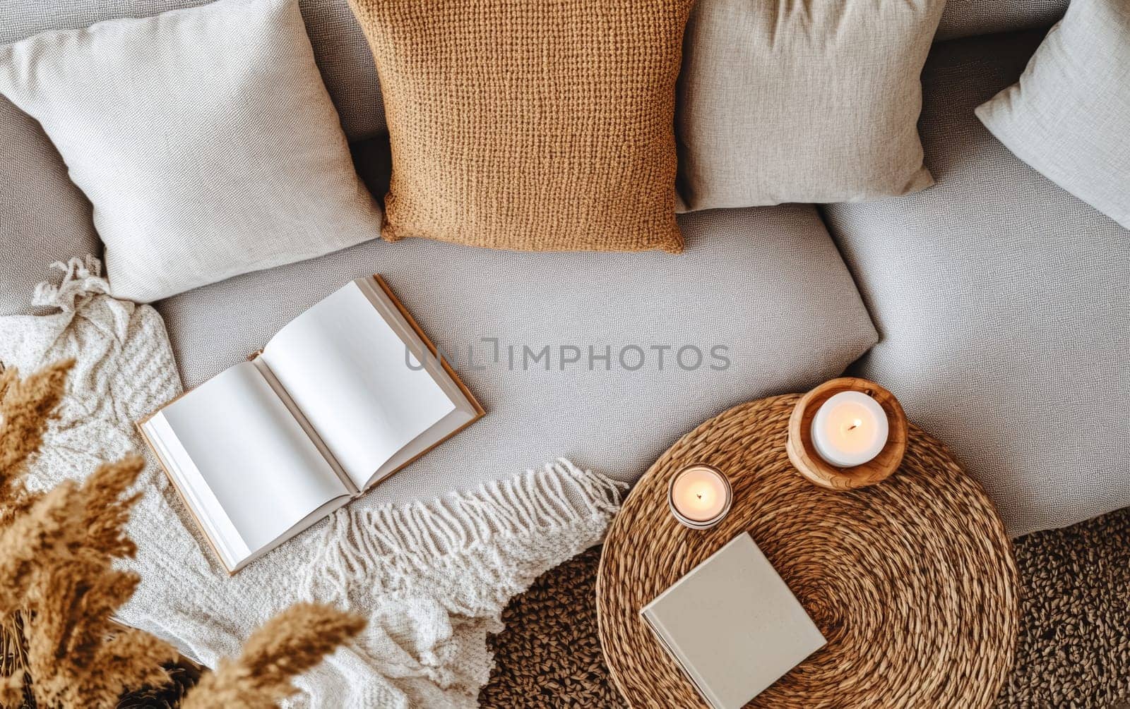 Inviting home interior featuring a comfortable sofa with pillows, open book, soft blanket, and glowing candles, creating a perfect atmosphere for relaxation and reading.
