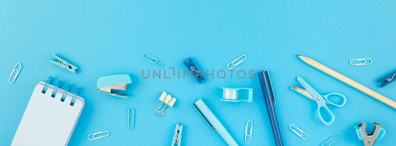 Top view flat lay of workspace desk styled design school and office supplies with copy space turquoise blue color paper background minimal style. Long wide banner Template feminine blog social media