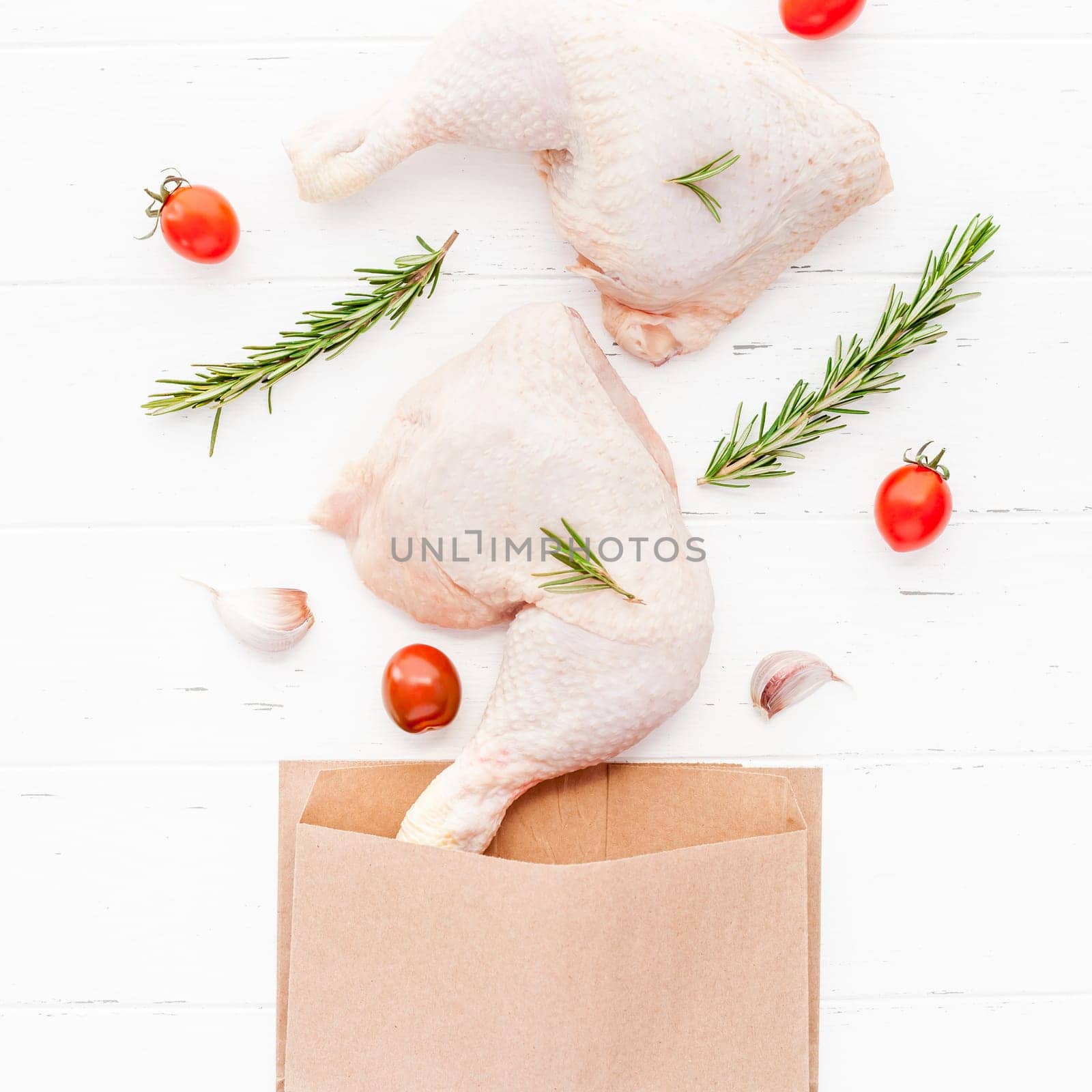 Creative Top view flat lay of fresh raw chicken legs with rosemary herbs garlic tomatoes on white wooden background with copy space. Food preparation recipe cooking concept