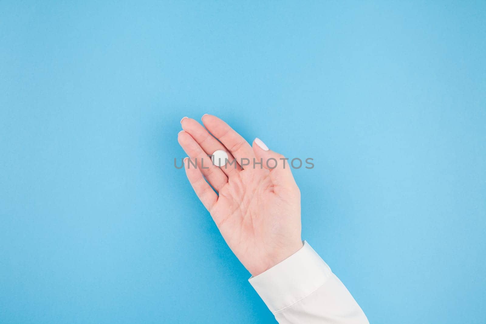 Woman hand holding a white pill on pastel blue paper background with copy space in minimal style, template for text. Concept of medical treatment, pharmacy, healthcare.