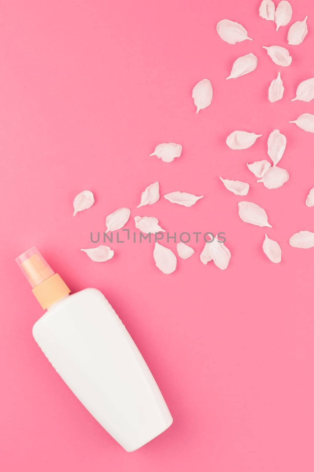 Flat lay set of sunscreen blank bottle mockup and white flowers petals on pastel pink color background for blog and social media with copy space for text