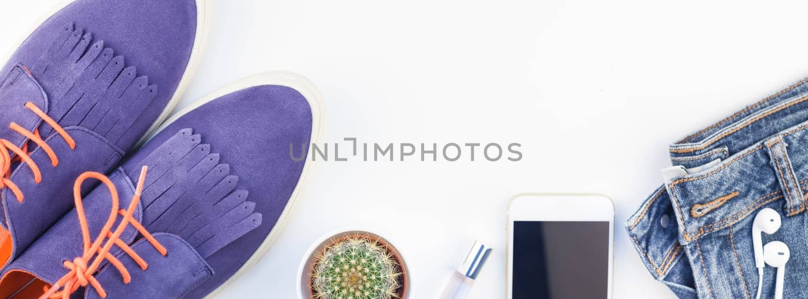 Long wide banner Flat lay of suede shoes, blue jeans, bracelets cactus and smartphone headphones on white background with copy space. Overhead view of woman casual outfit. Trendy hipster look top view