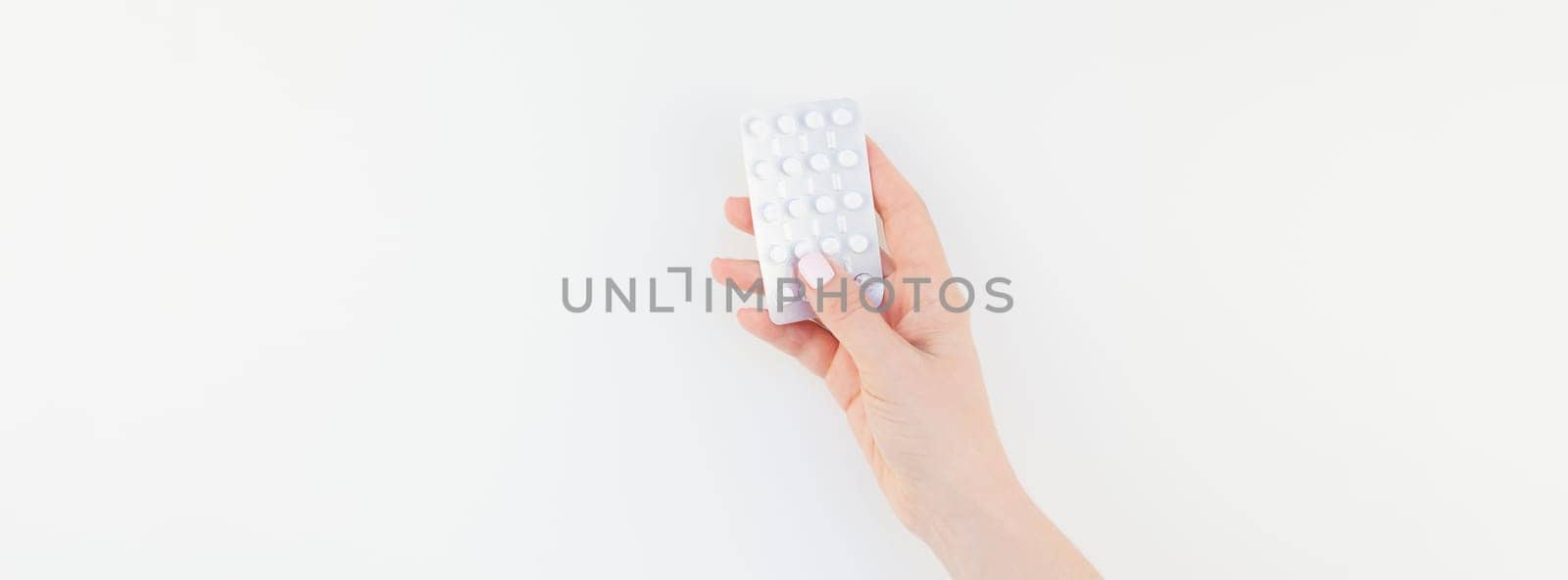 Woman hand with pastel manicure polish holding pills in blister isolated on white background with copy space. Long wide banner for feminine beauty blog social media. Female healthcare concept