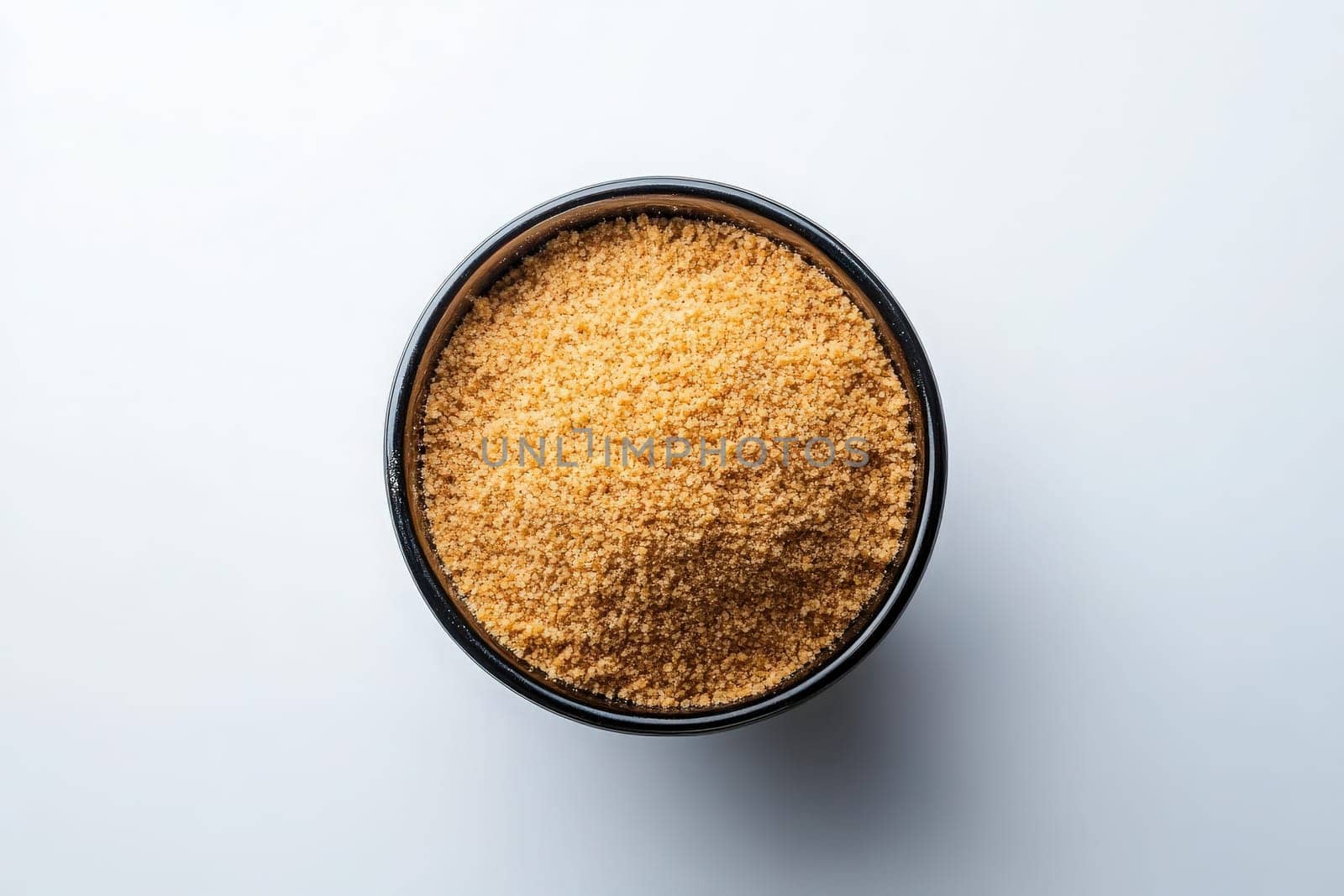 A black bowl filled with finely crushed graham cracker crumbs is prominently displayed on a light surface, showcasing the golden-brown texture and fine consistency of the crumbs.