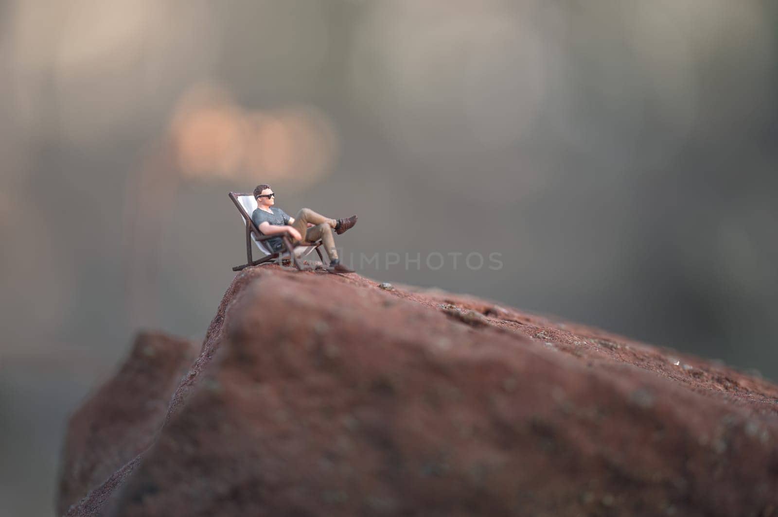 Miniature man in casual clothing relaxing on a deckchair on top of a mountain