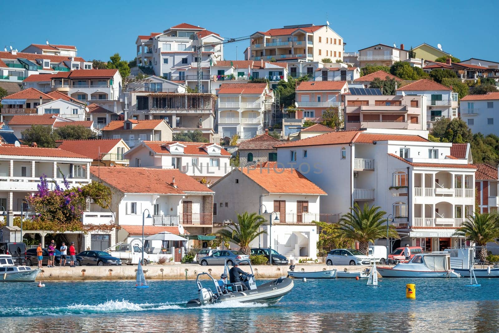 Rogoznica, Croatia - October 31, 2022: Tourists are enjoying a sunny day while driving a motorboat in front of the picturesque coastal town of Rogoznica, Croatia