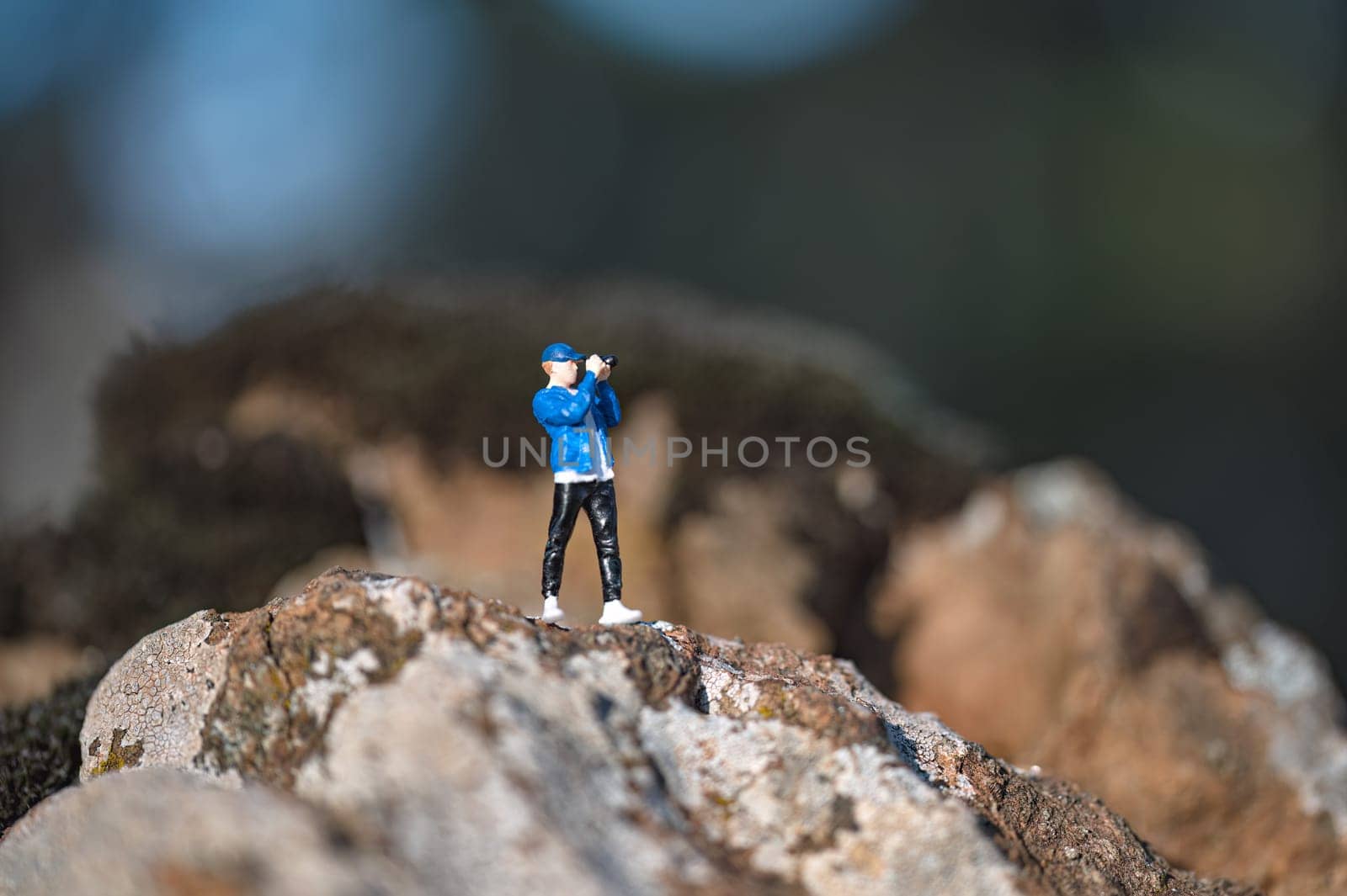 Miniature photographer is taking nature pictures while standing on rocks on a sunny day