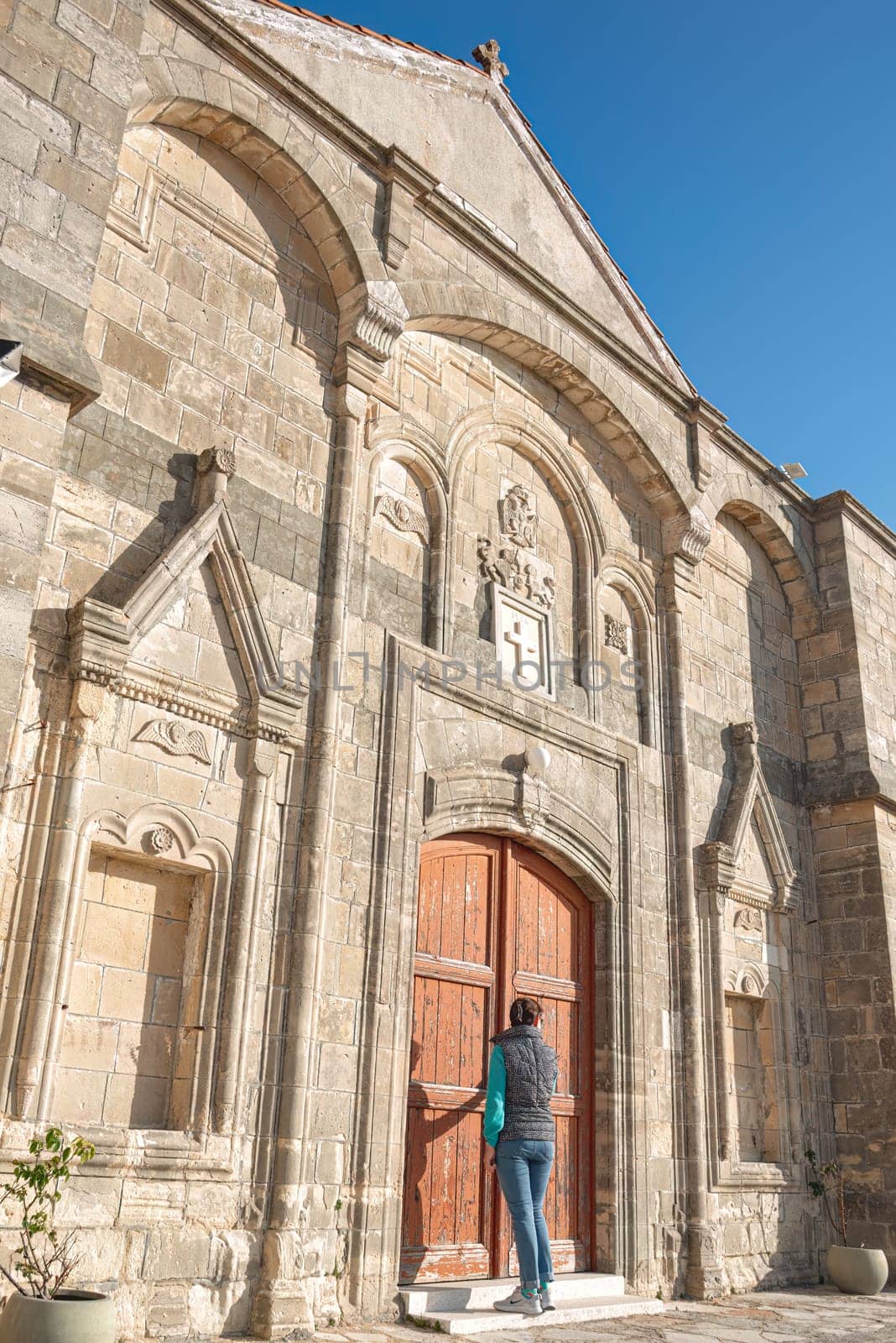 Tourist entering the stone church of Timios Prodromos in Vouni village, on a sunny day with clear blue sky. Limassol District, Cyprus