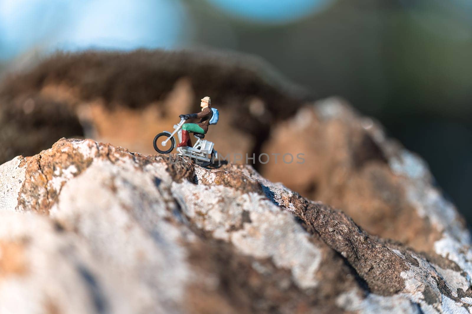 Miniature figurine of a person wearing a backpack is riding a motorcycle up a rocky mountain