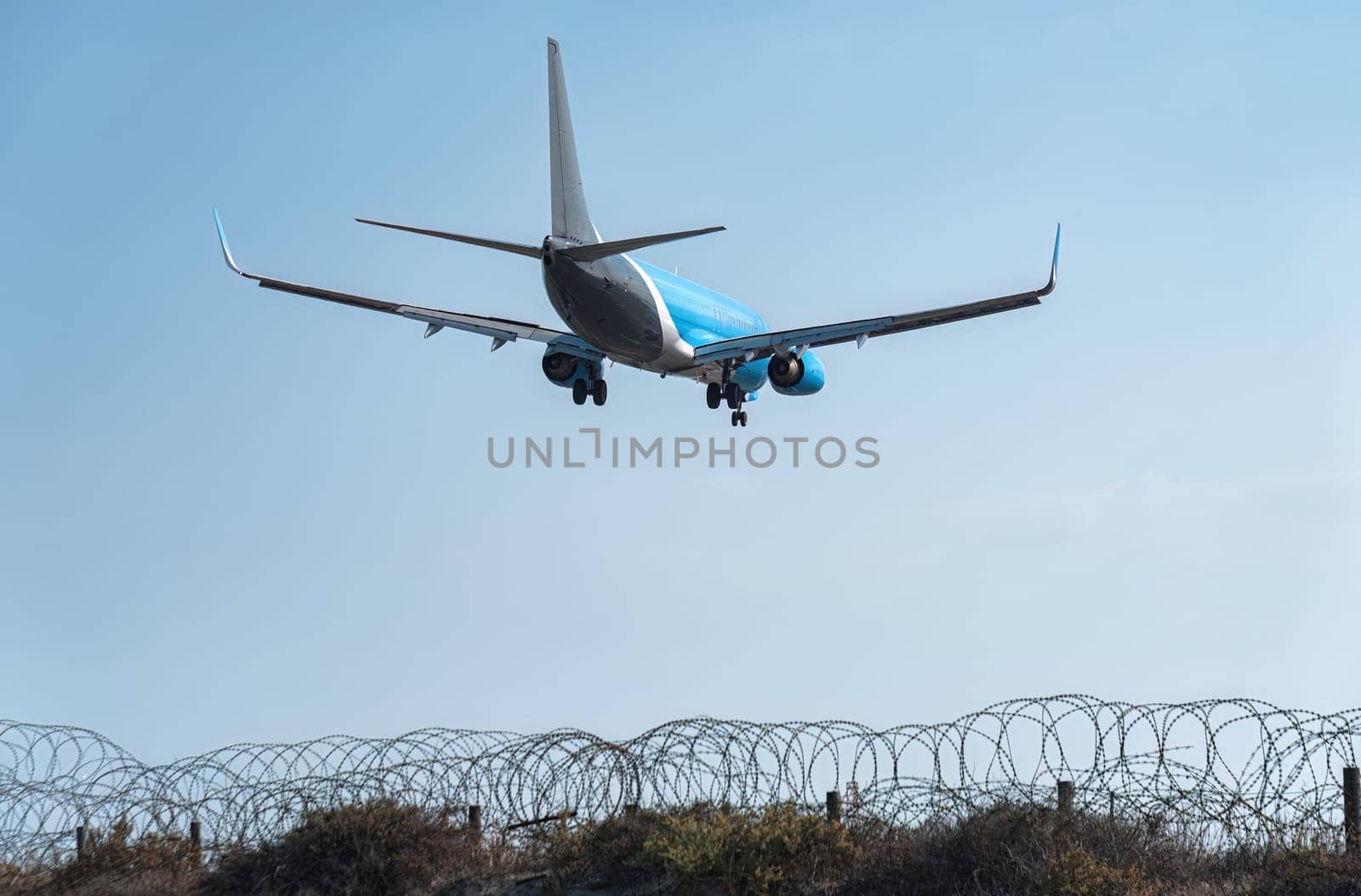 Passenger airplane is landing at an airport behind a barbed wire fence