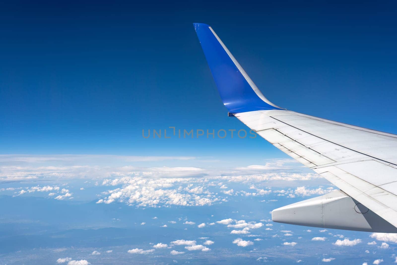 Airplane is flying high above the earth with a view of the clouds and blue sky