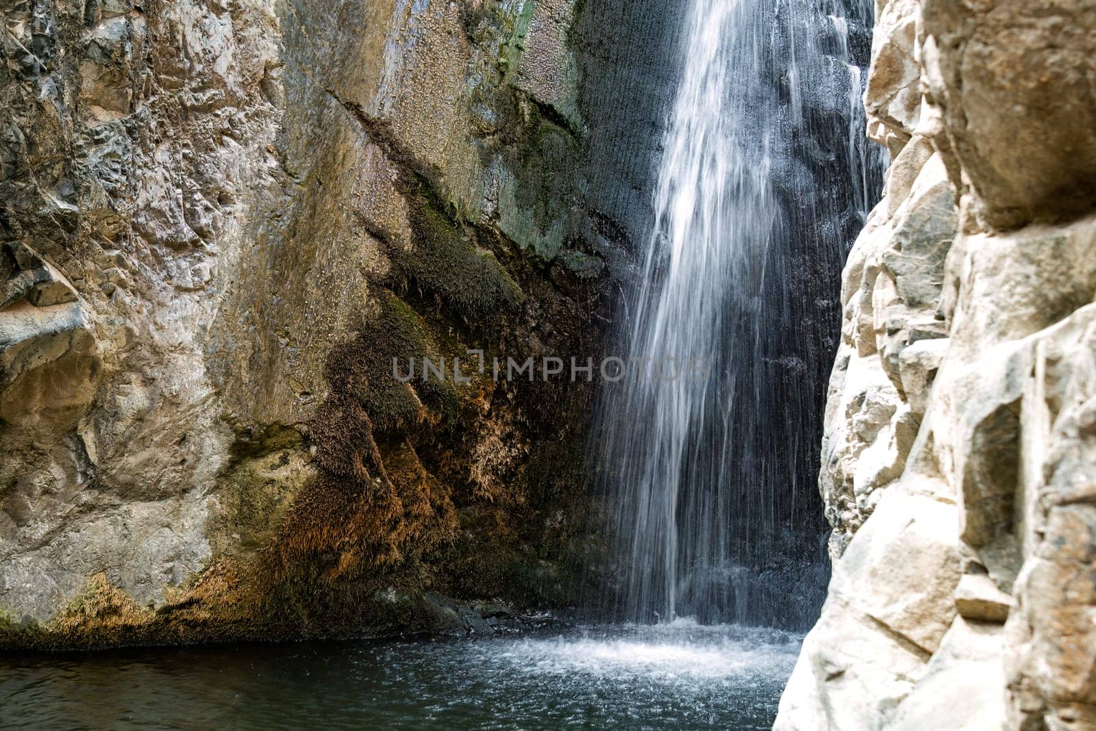 Water is falling from the top of a cliff into a pool of water at the Millomeris waterfalls. Cyprus