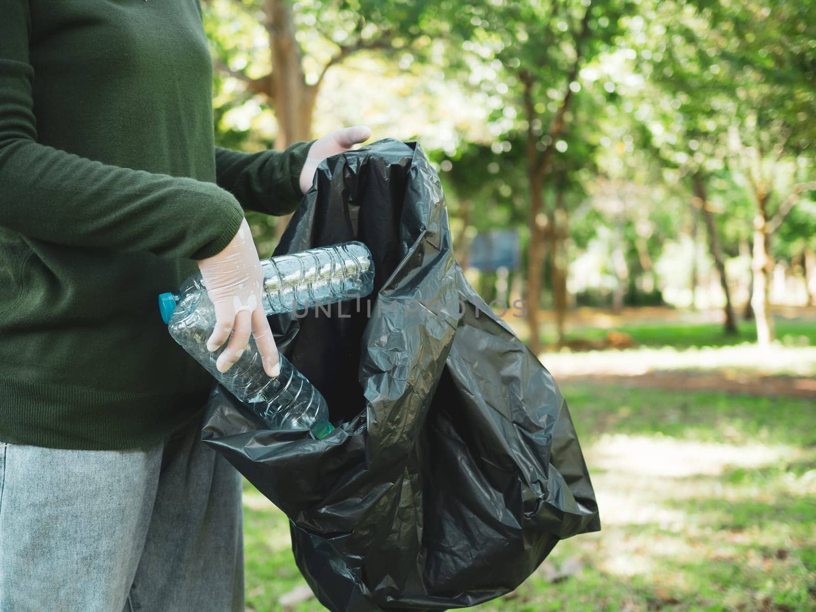 Woman of dedicated volunteers are participating in an environmental cleaning activity in a park. Woman wearing gloves and hold large black bags. Woman collecting trash and plastic bottles in a park.