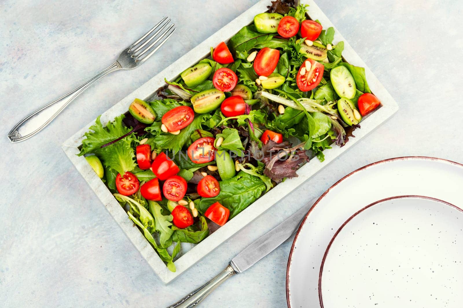 Summer vegan salad with tomatoes, nut and green on a stone tray. Healthy tomatoes salad on a stone plate