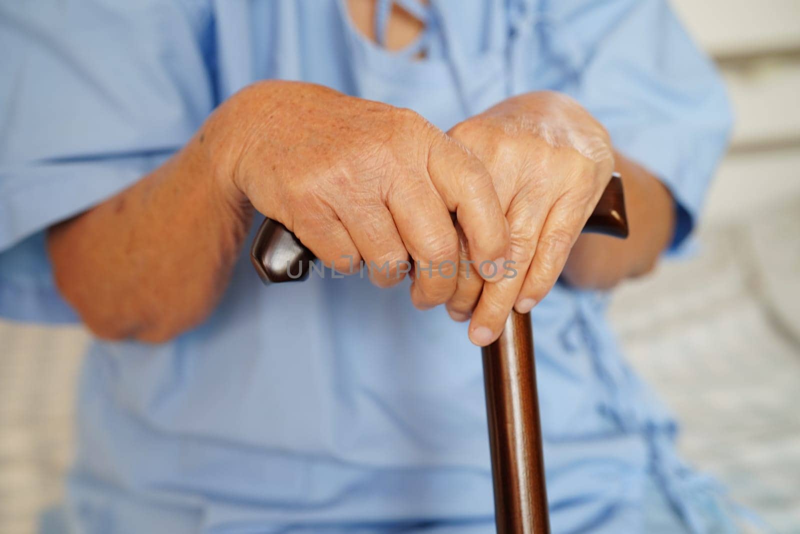 Asian elderly disability woman patient holding walking stick in wrinkled hand at hospital.