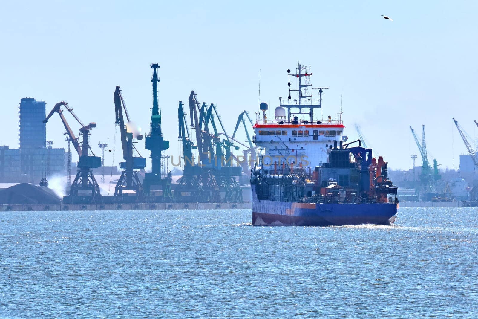 View of commercial cargo port and its container bridge cranes and a ship entering port on a sunny day.