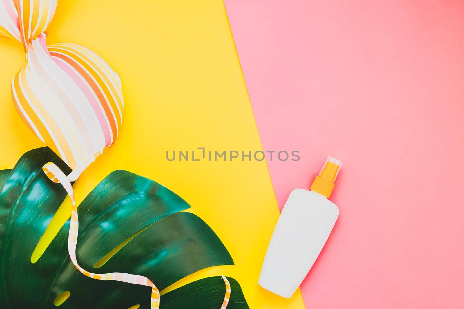 Tropical jungle palm monstera leaves, sunglasses, sunscreen blank bottle mockup and woman's swimsuit top on bright color paper background. Summer vacations creative flat lay concept template for text