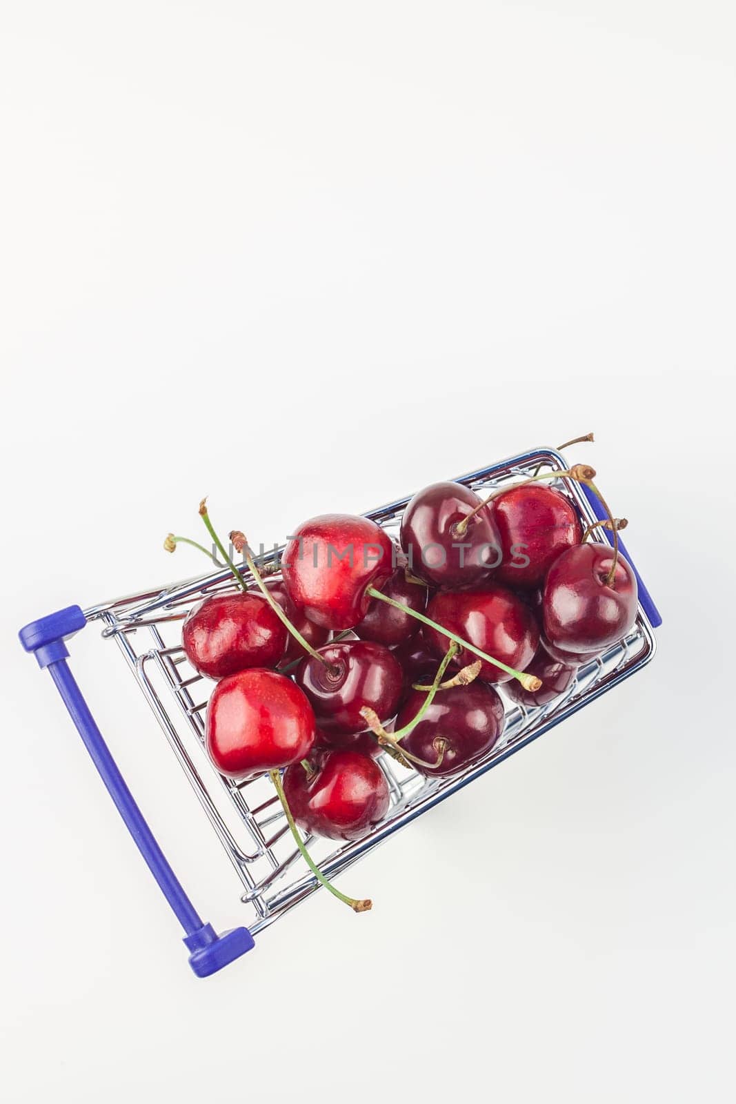 Creative top view of ripe cherries in a shopping cart with copy space isolated on white background in minimal style. Concept of supermarket or fruit market shopping. Template for your text or design.